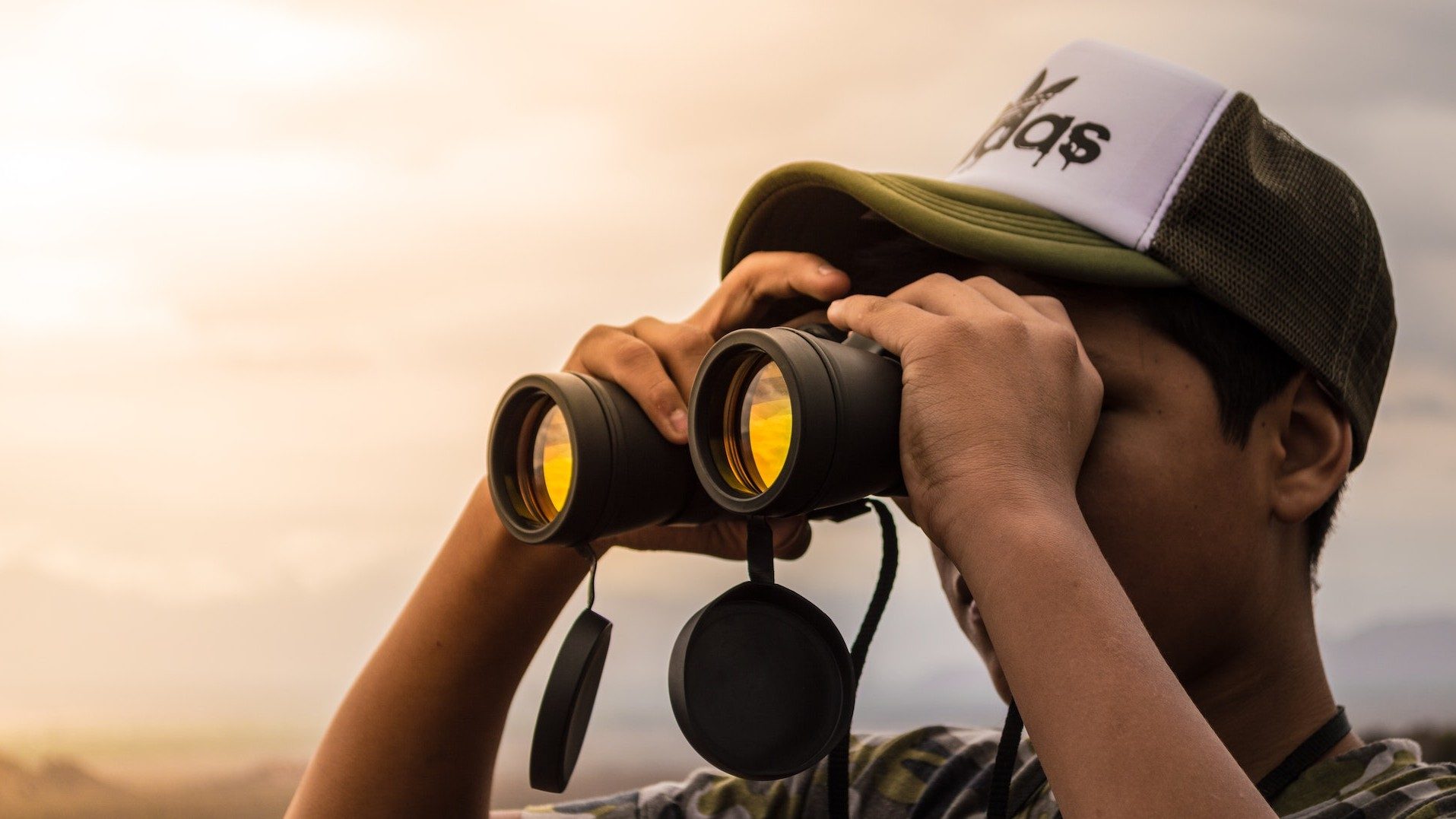 Ein Mann mit Adidas-Kappe blickt im Sonnenuntergang durch ein Fernglas in die Ferne