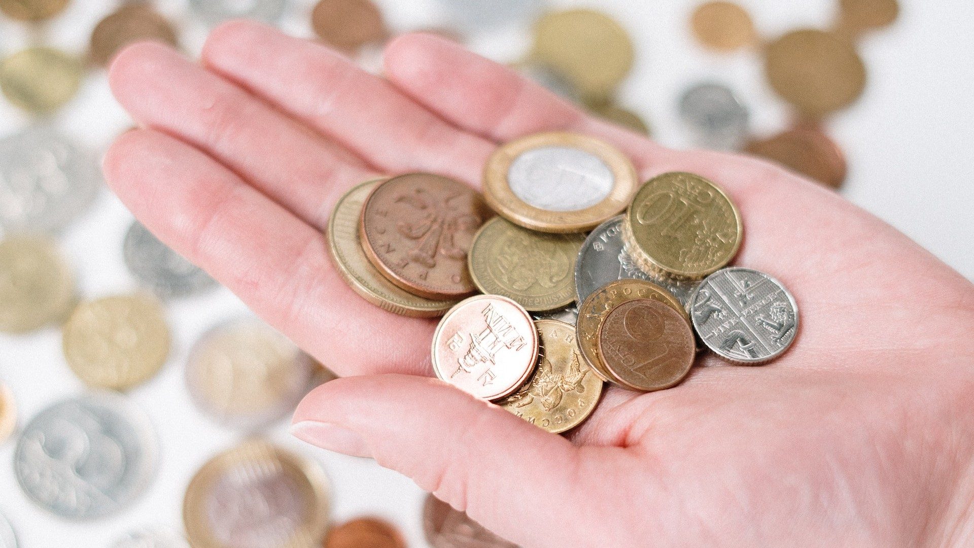 Eine Person hält Münzen verschiedener Währungen in einer Hand