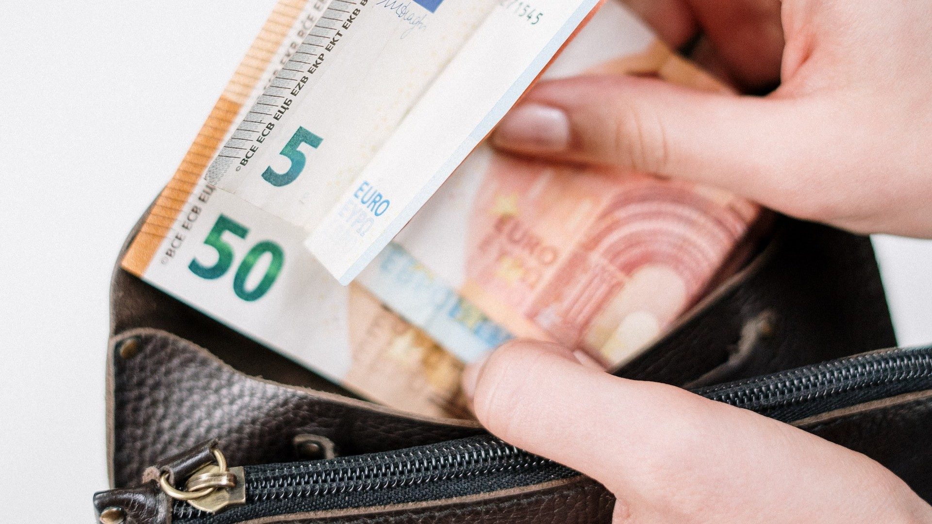 Eine Person steckt mehrere Euro-Scheine in eine Geldbörse