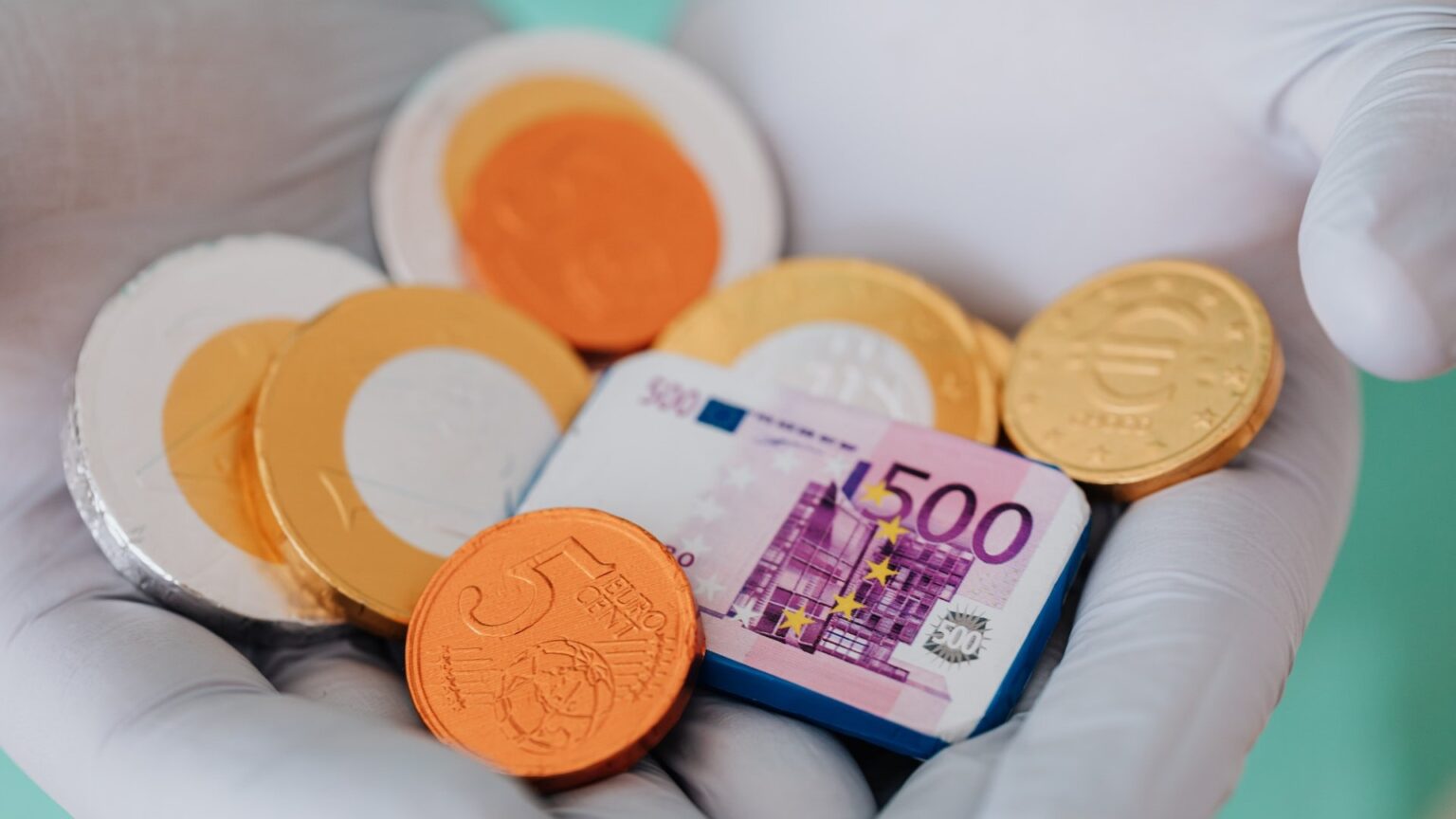 Eine Person mit weißen Handschuhen hält Schokoladen-Euros als Münzen und Scheine