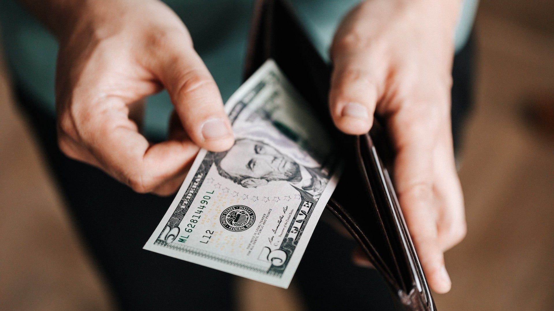 Eine Person holt einen Fünf-Dollar-Schein aus dem Geldbeutel