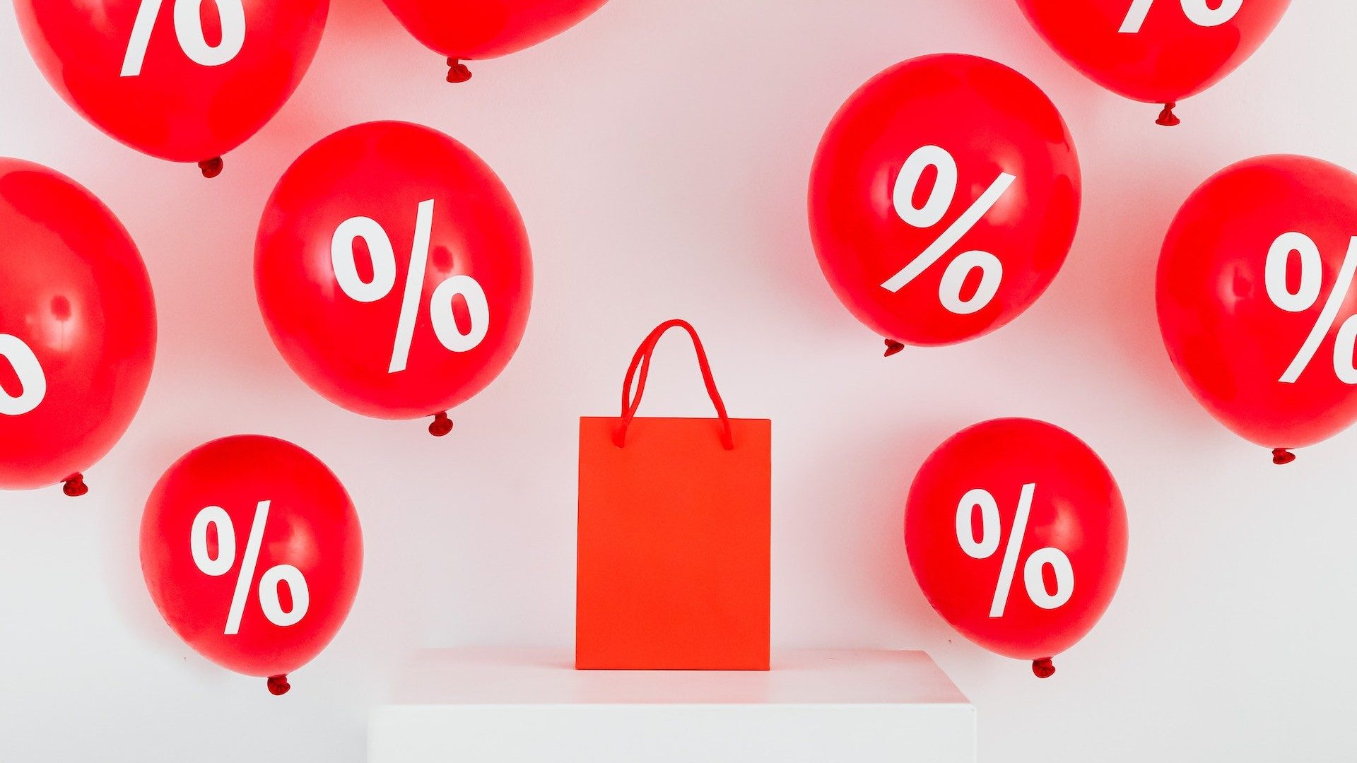Eine rote Einkaufstüte ist umgeben von roten Ballons mit Prozent-Zeichen