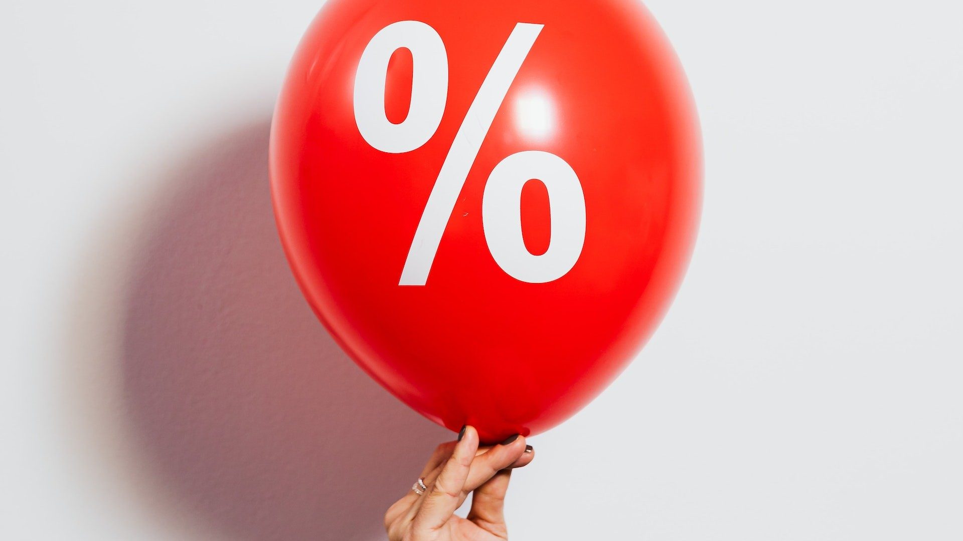 Eine Person hält einen roten Ballon mit großem Prozent-Zeichen