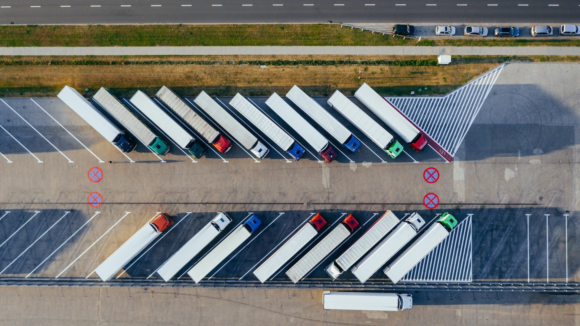 Mehrere beladene Lkw stehen auf einem Parkplatz neben einer Schnellstraße