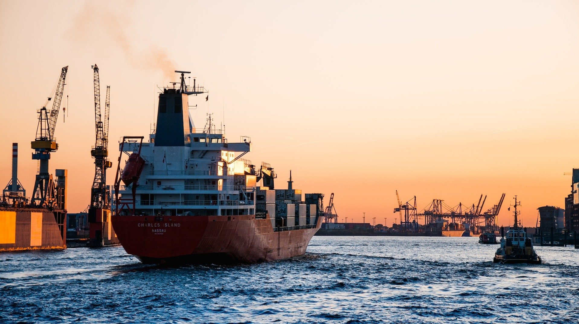Ein voll beladenes Containerschiff fährt bei Sonnenuntergang durch den Hafen