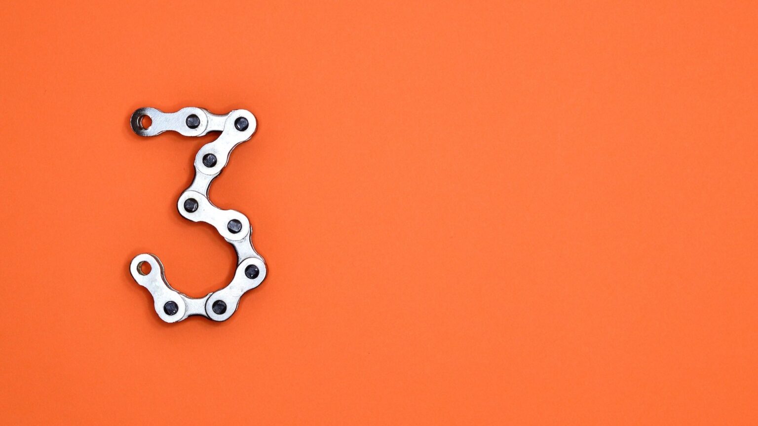 Glieder einer Fahrradkette zeigen auf orangem Untergrund die Zahl drei