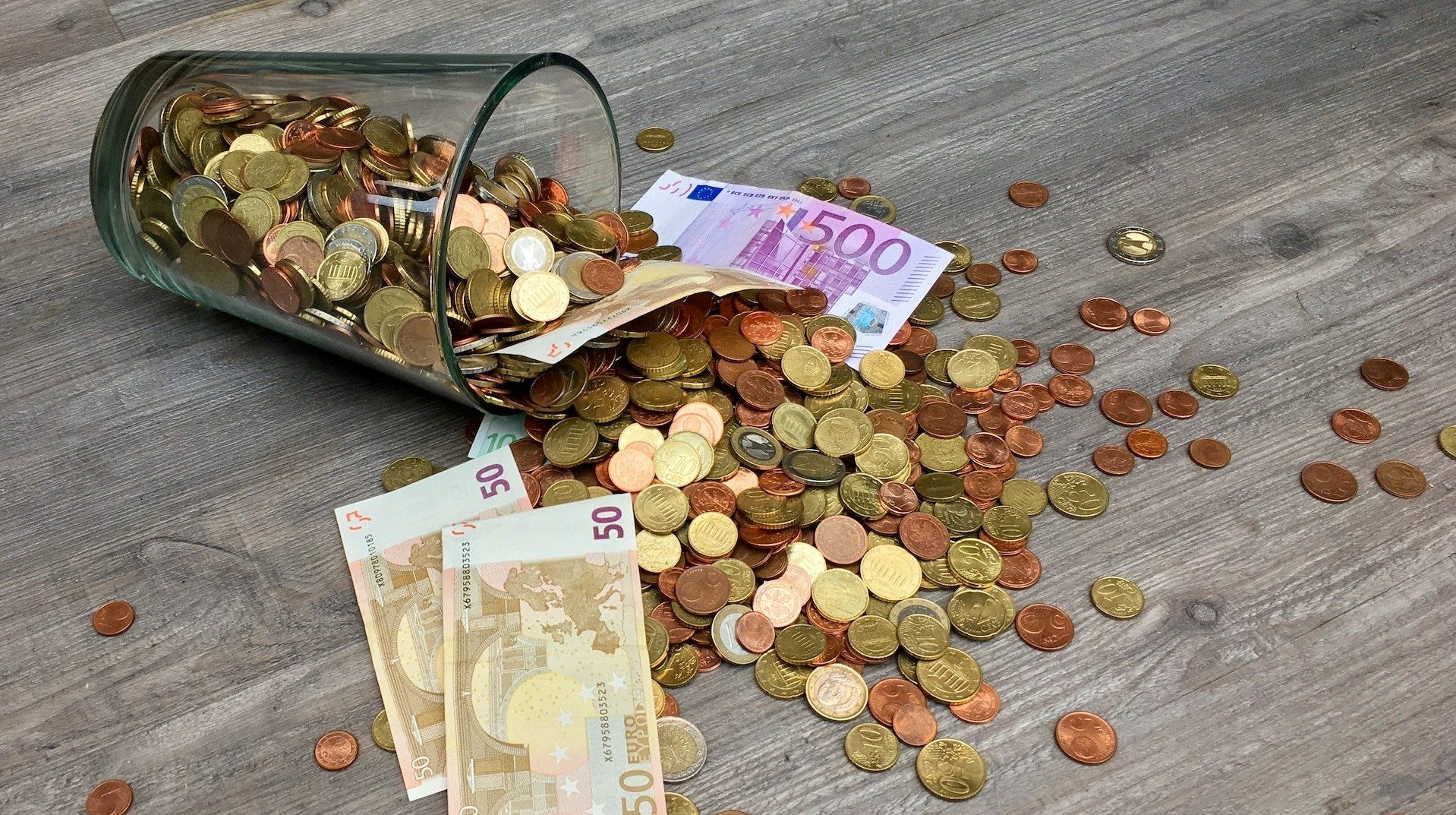 Auf einem umgestoßenen Glas sind Euro-Münzen und -Geldscheine herausgefallen
