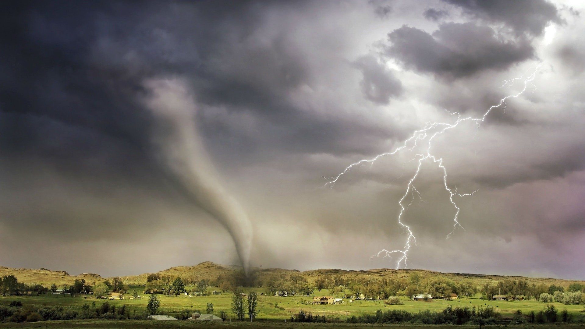 Während ein Tornado über eine Landschaft fegt, schlägt unweit ein Blitz ein