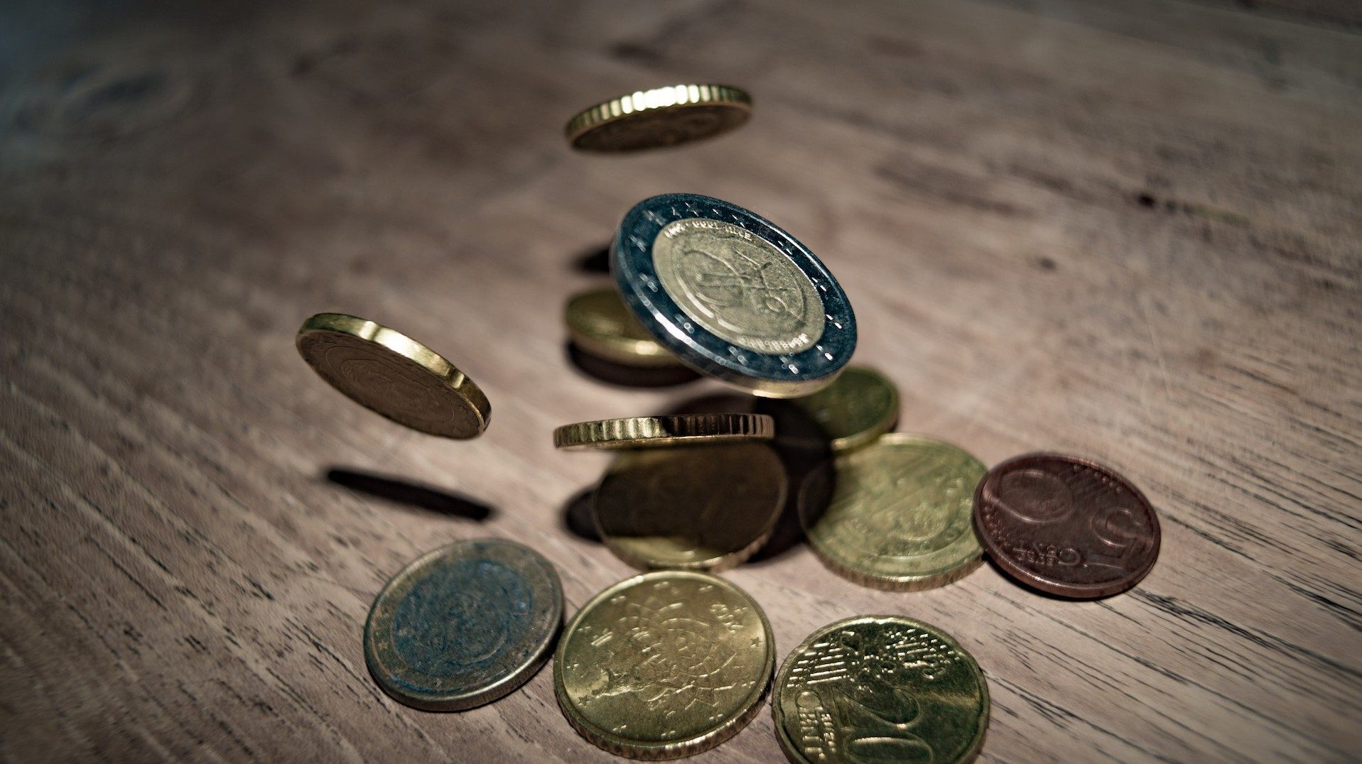 Euro- und Cent-Münzen fallen auf einen Holztisch