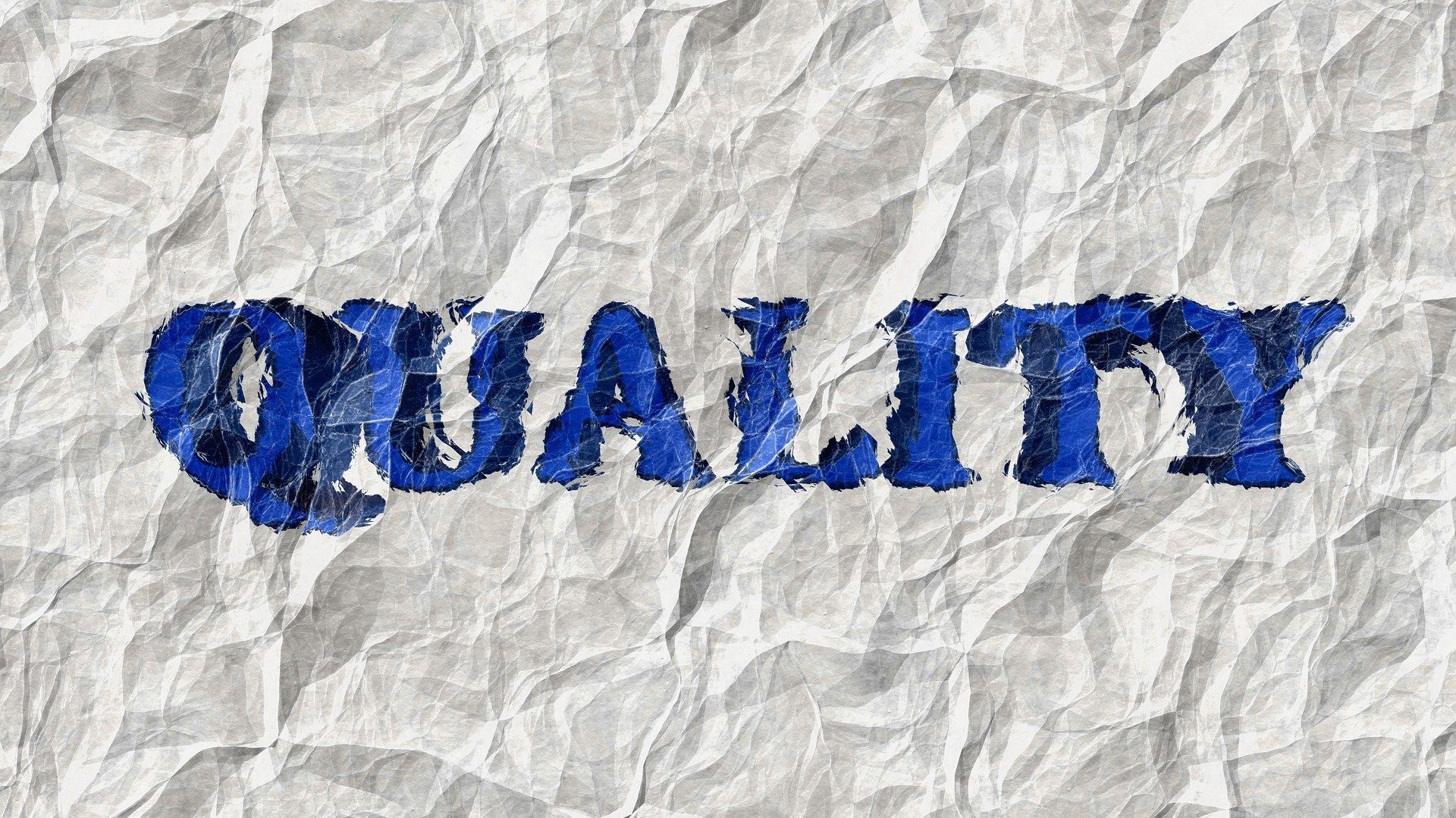 Schriftzug "Quality" in blau auf einem zerknitterten Blatt Papier