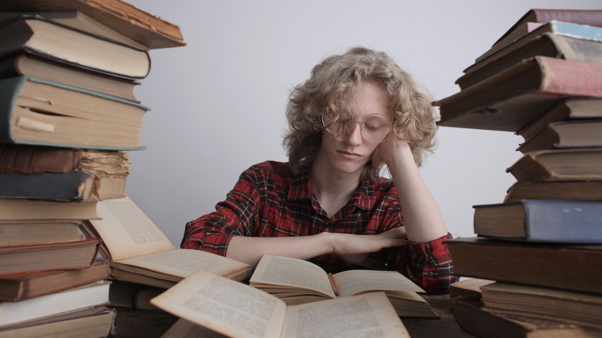 Eine junge Frau liest aus einem Buch, umgeben von dutzenden anderen dicken Büchern