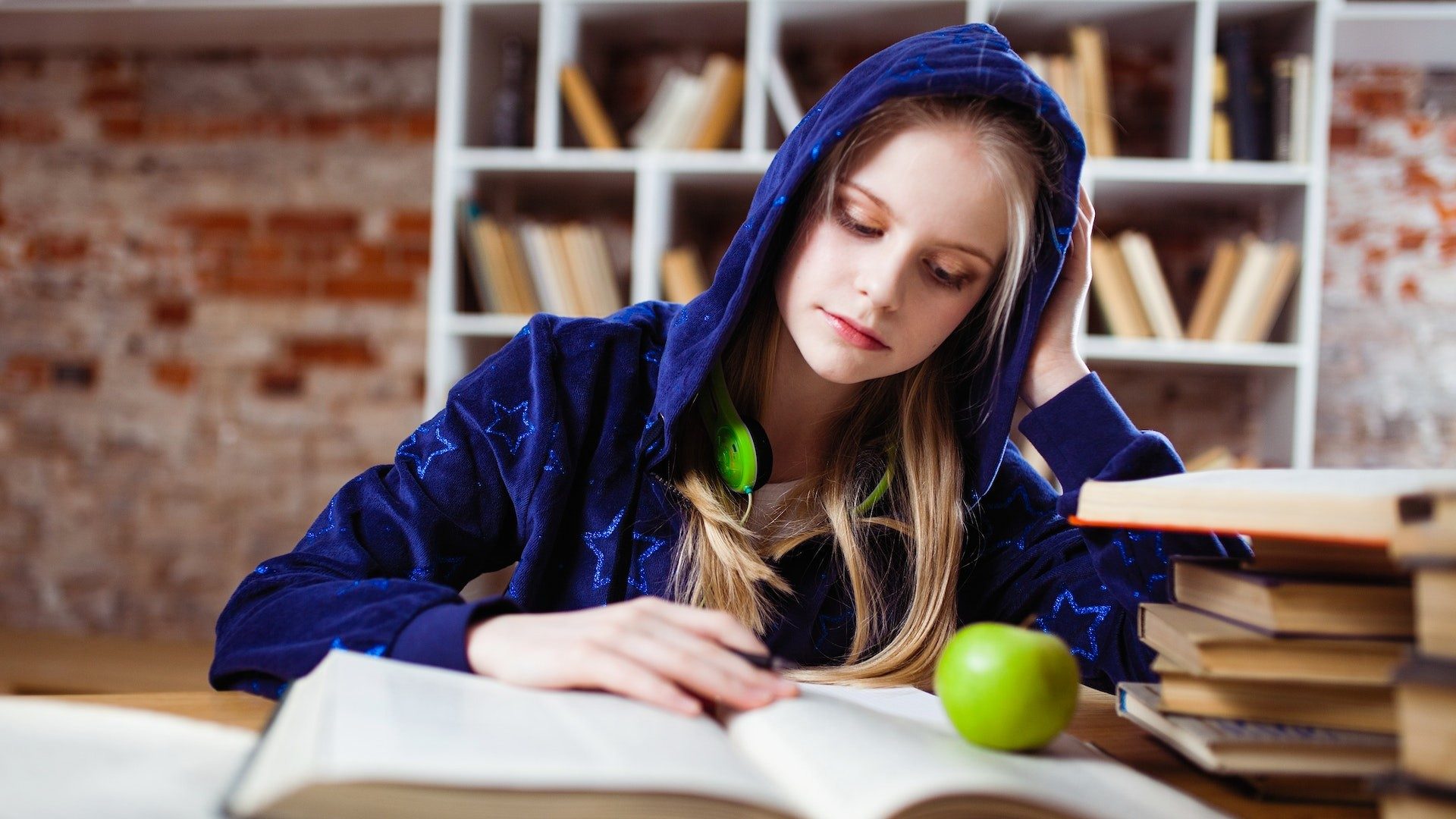 Ein Mädchen lernt für die Schule, auf ihrem Schulbuch liegt ein grüner Apfel