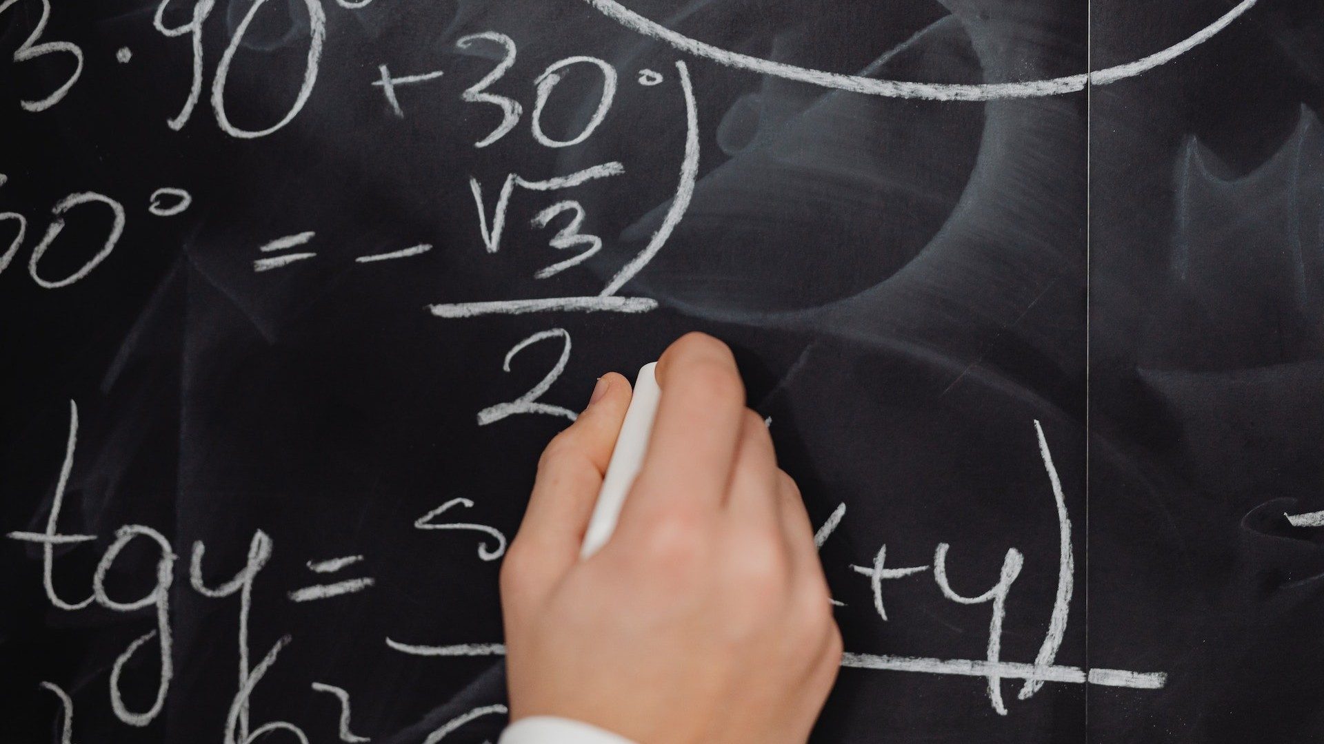 Eine Person schreibt mit Kreide mathematische Formeln an eine Tafel