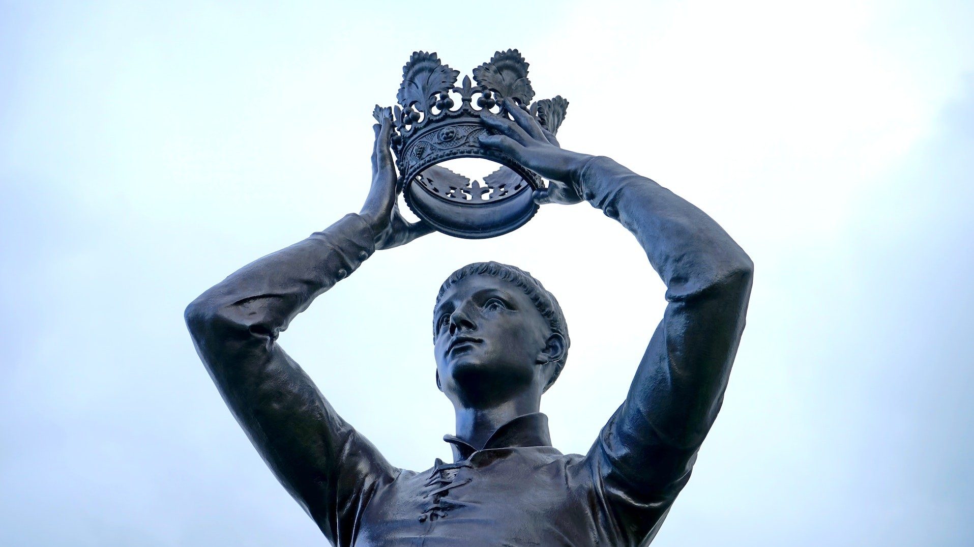 Statue eines Mannes, der seine Krone in den Händen über dem Kopf hält