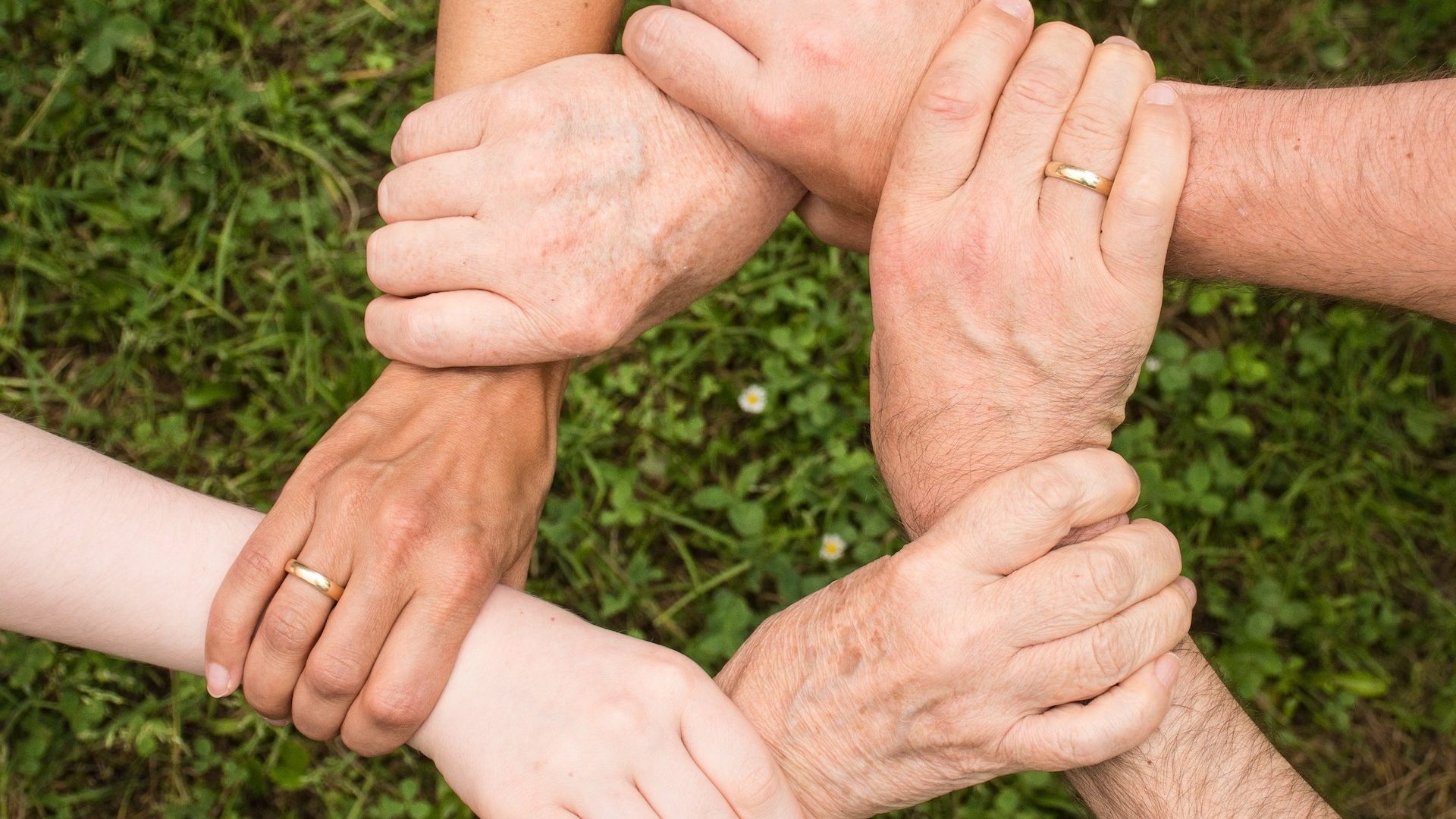 Hände von sechs Menschen verschiedener Generationen halten sich gegenseitig fest