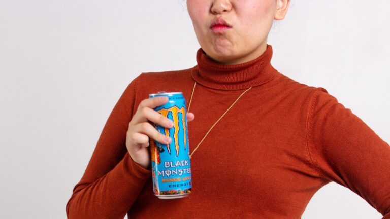 Eine Frau mit rotem Pullover hält eine Monster Energy-Getränkedose in der Hand