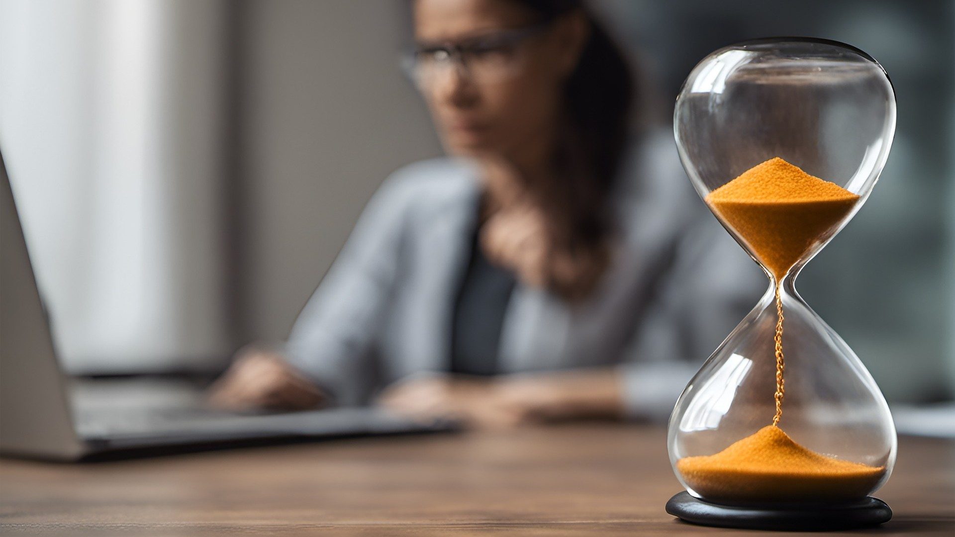 Eine Sanduhr in Nahaufnahme auf einem Tisch, an dem eine Person arbeitet