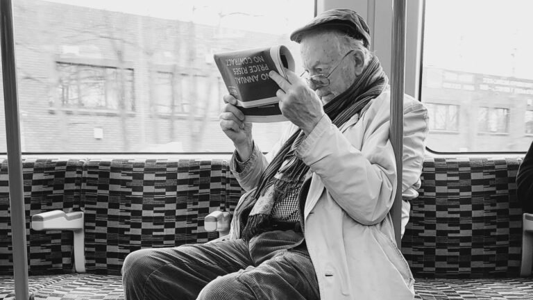 Ein älterer Mann mit Brille liest in einer Straßenbahn die Zeitung