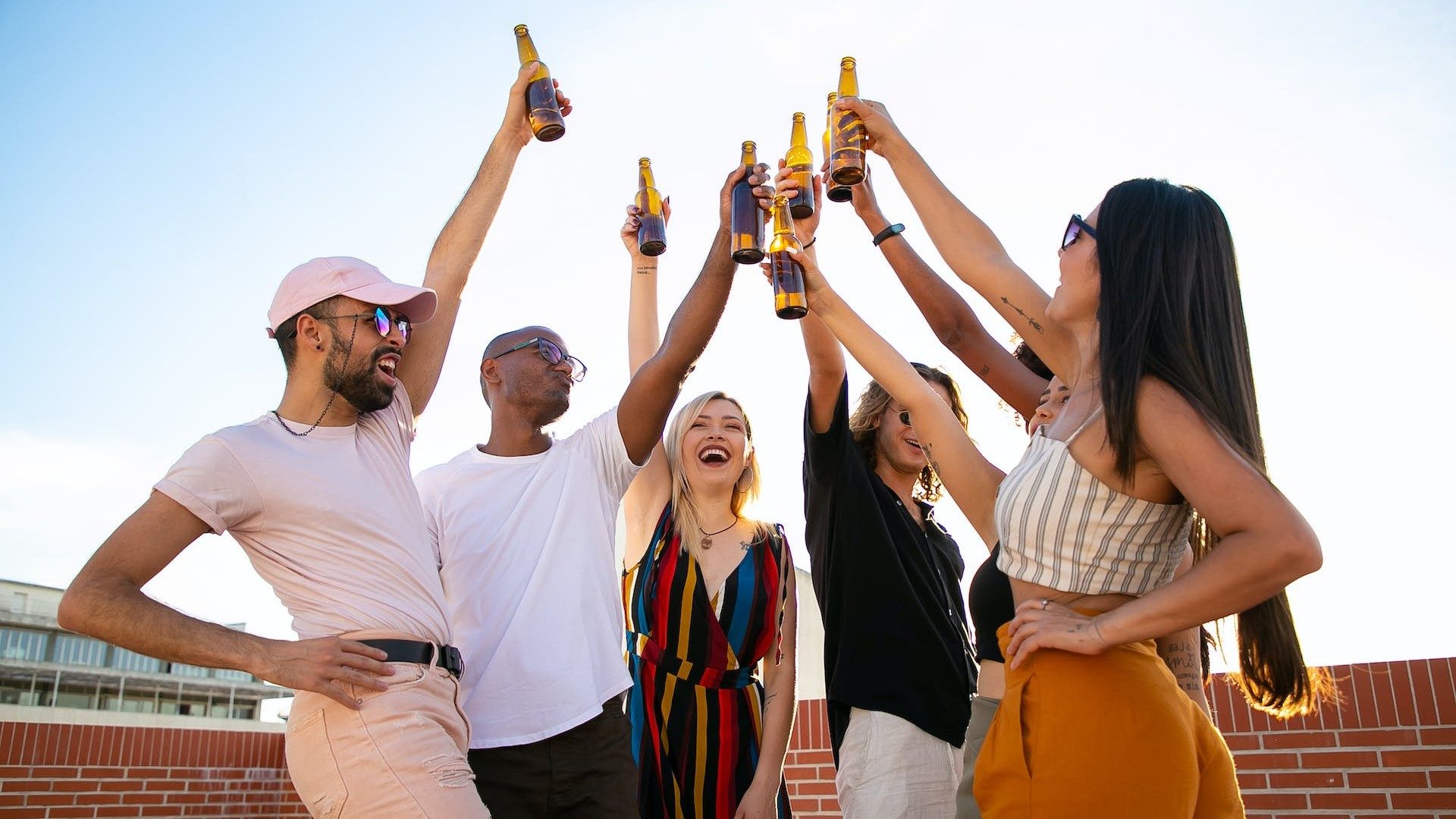 Eine Gruppe junger Leute stößt draußen mit einem Bier an