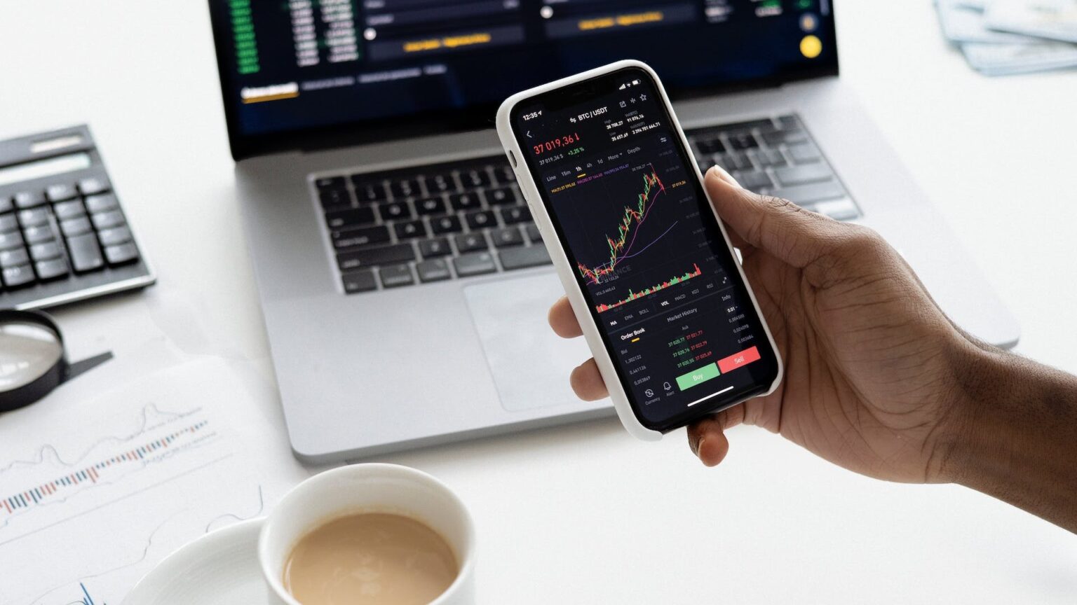 Eine Person hält ihr Smartphone in die Kamera, darauf ist der Bitcoin-Kursverlauf zu sehen