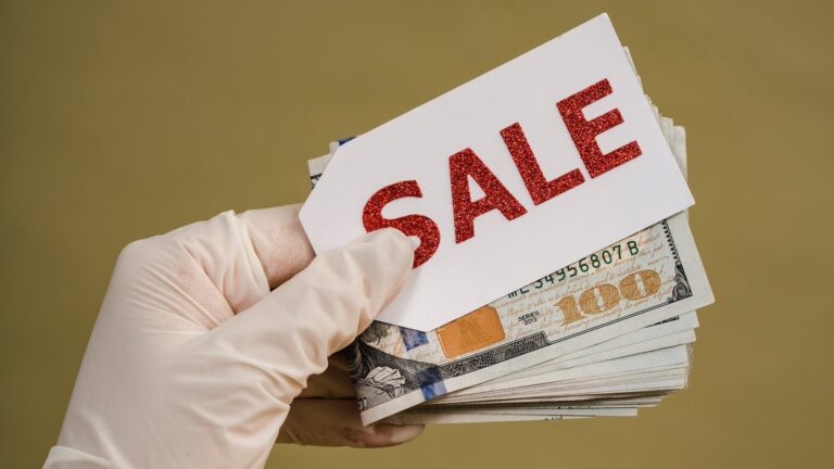 Eine Person hält ein Bündel Geld und ein Etikett mit der Aufschrift "Sale" in der Hand