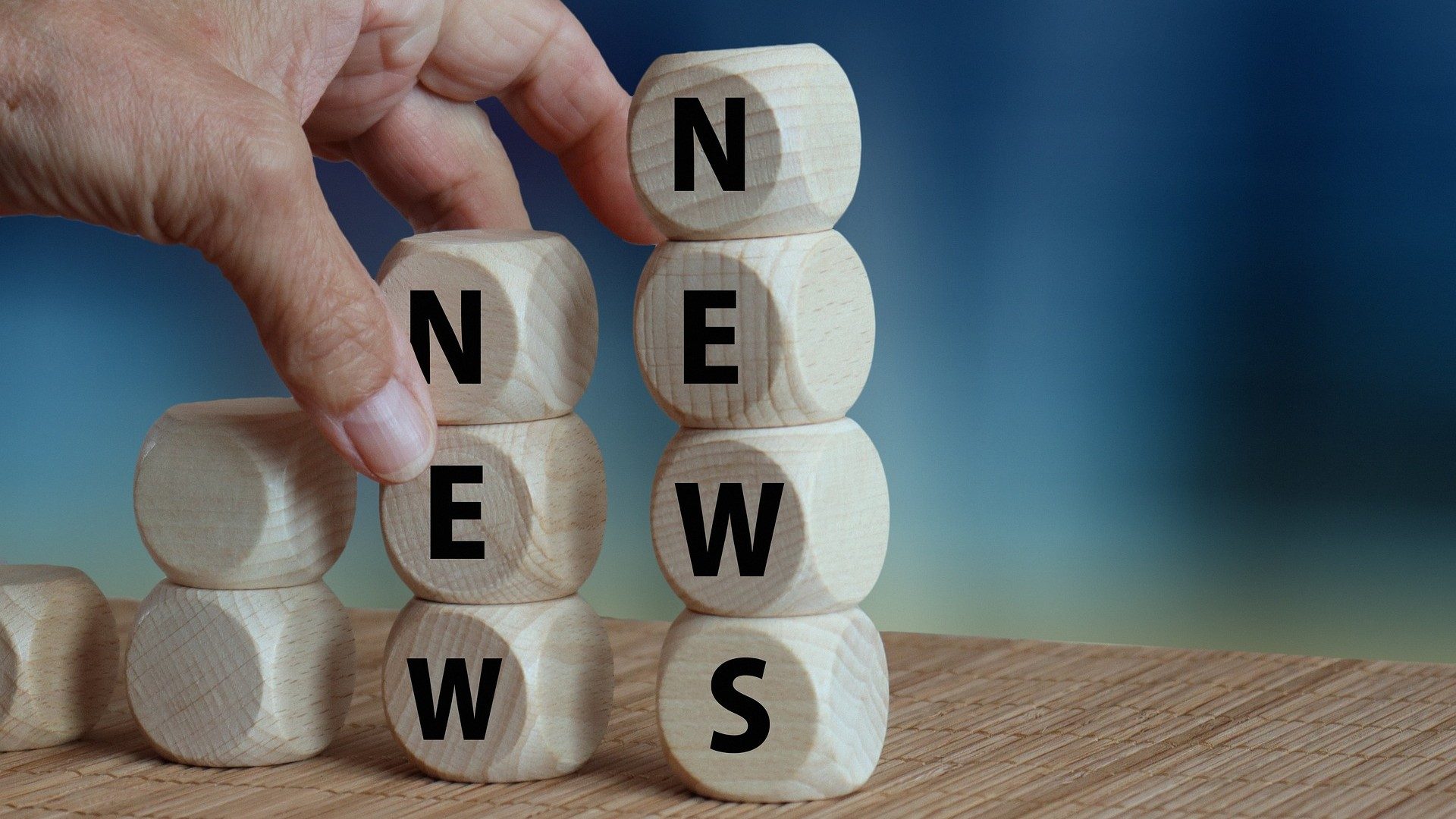 Eine Hand stapelt Holzklötze aufeinander, die das Wort "News" buchstabieren