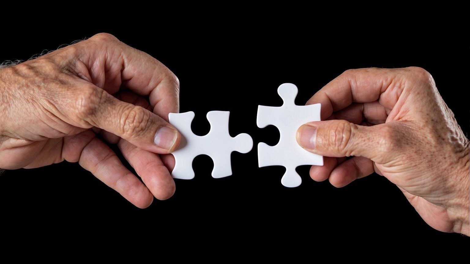 Zwei ältere Menschen halten weiße Puzzleteile aneinander, die zusammenpassen