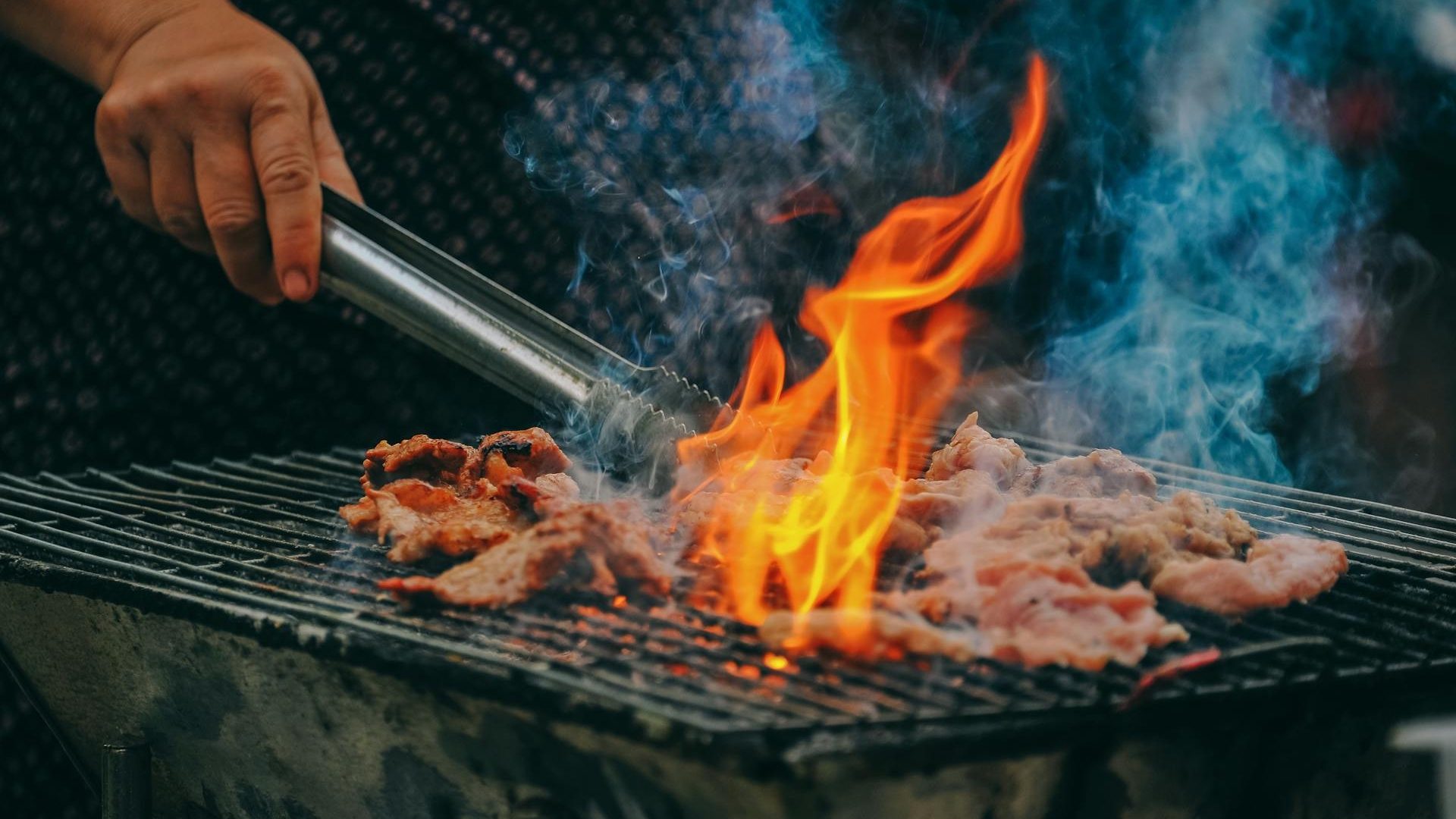 Flammen züngeln um Fleisch, das auf einem Grill liegt.