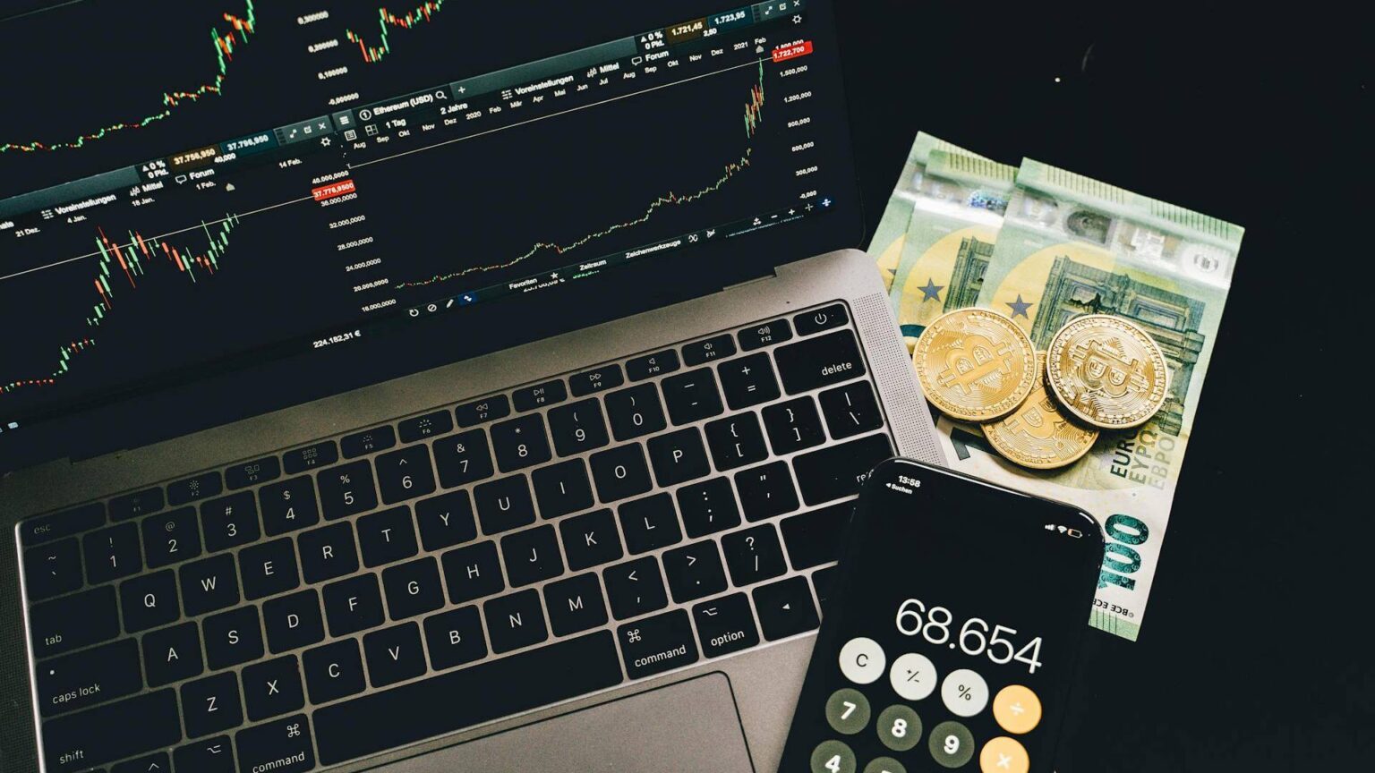 Charts verschiedener Kryptowährungen auf einem Bildschirm, daneben drei goldene Bitcoins
