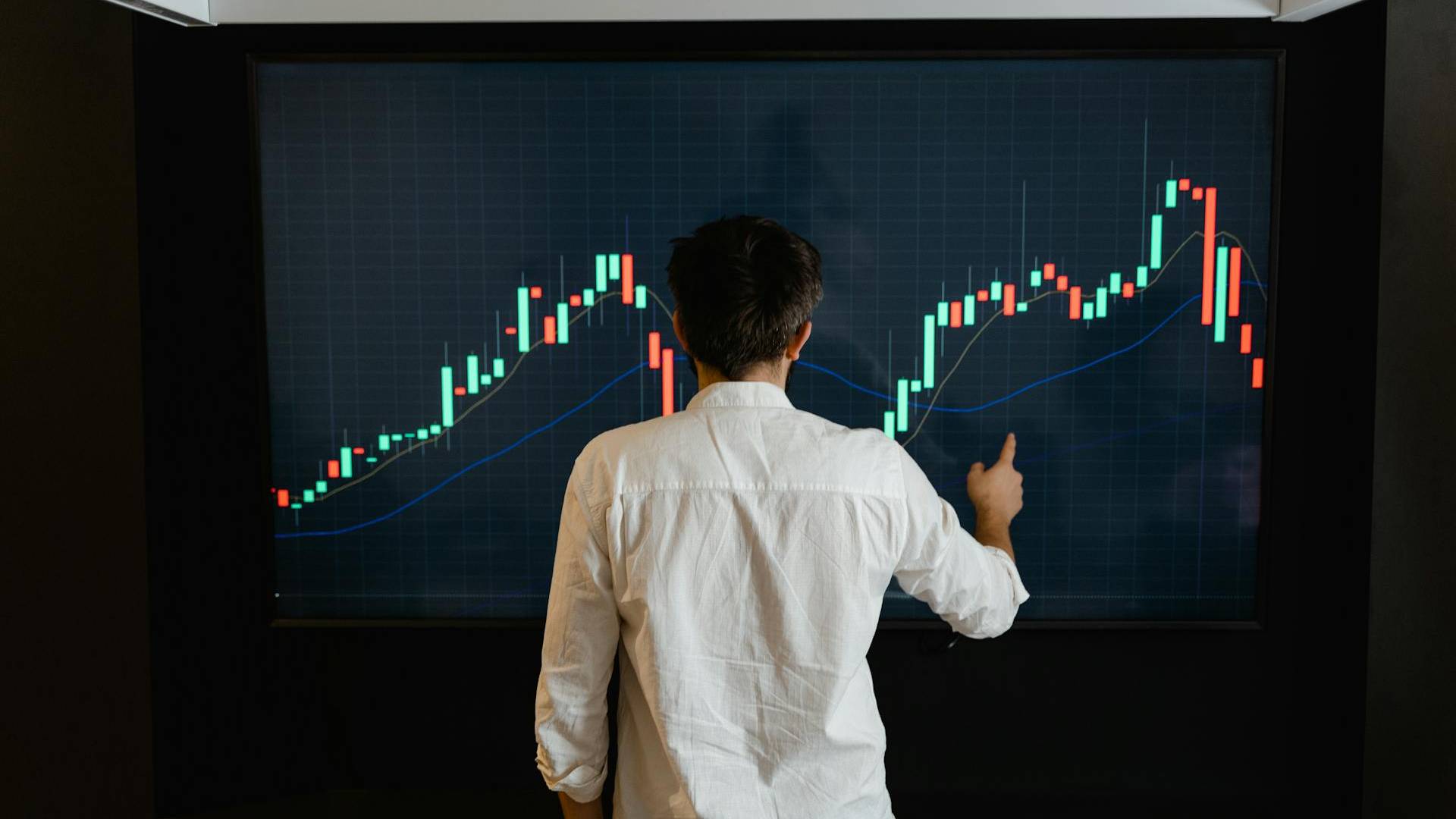 Ein Mann im weißen Hemd steht vor einem Candlestick-Chart